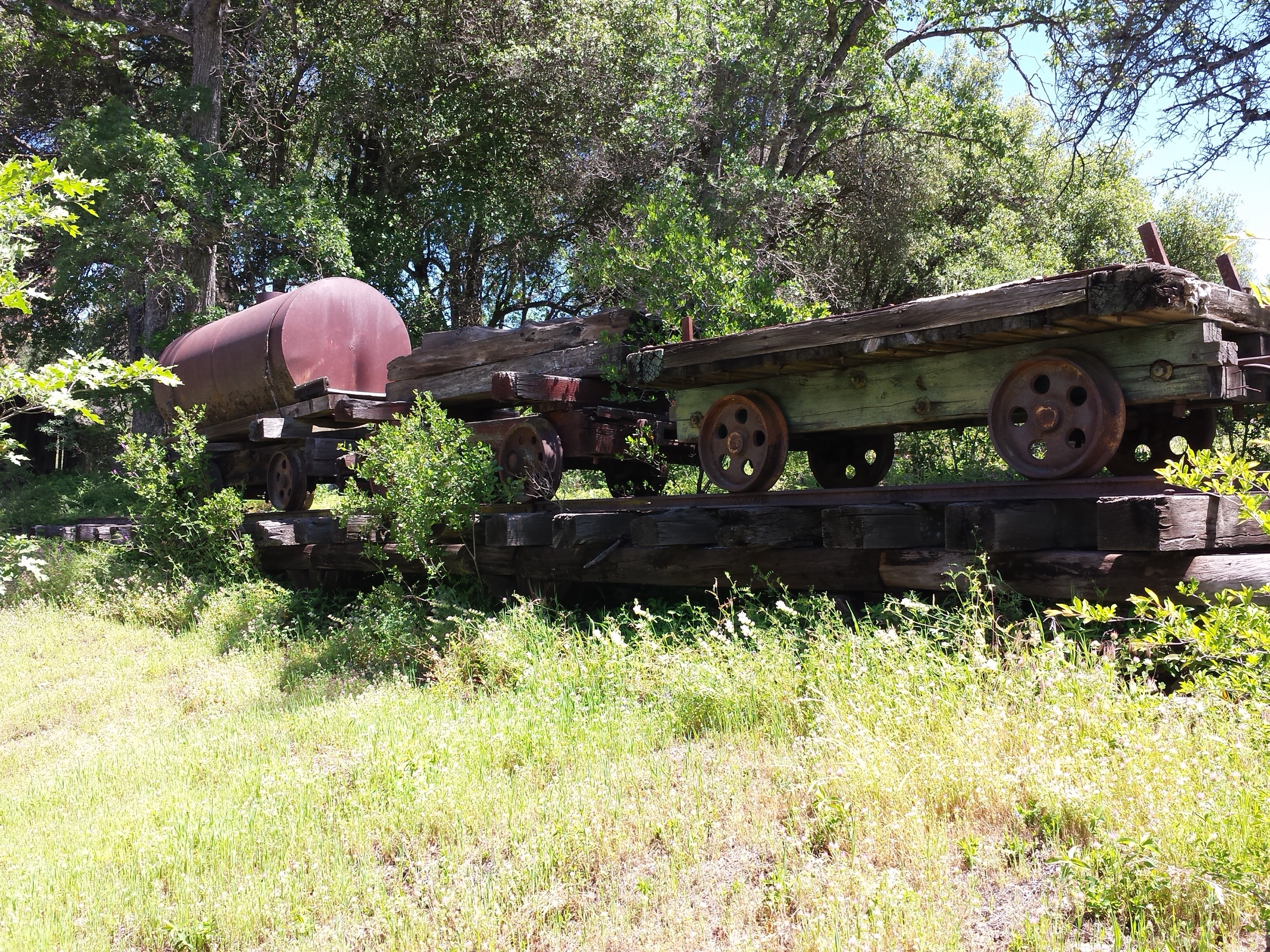 Rusting logging railroad flatcars and a tank car on stacked ties among oaks in Tuolumne