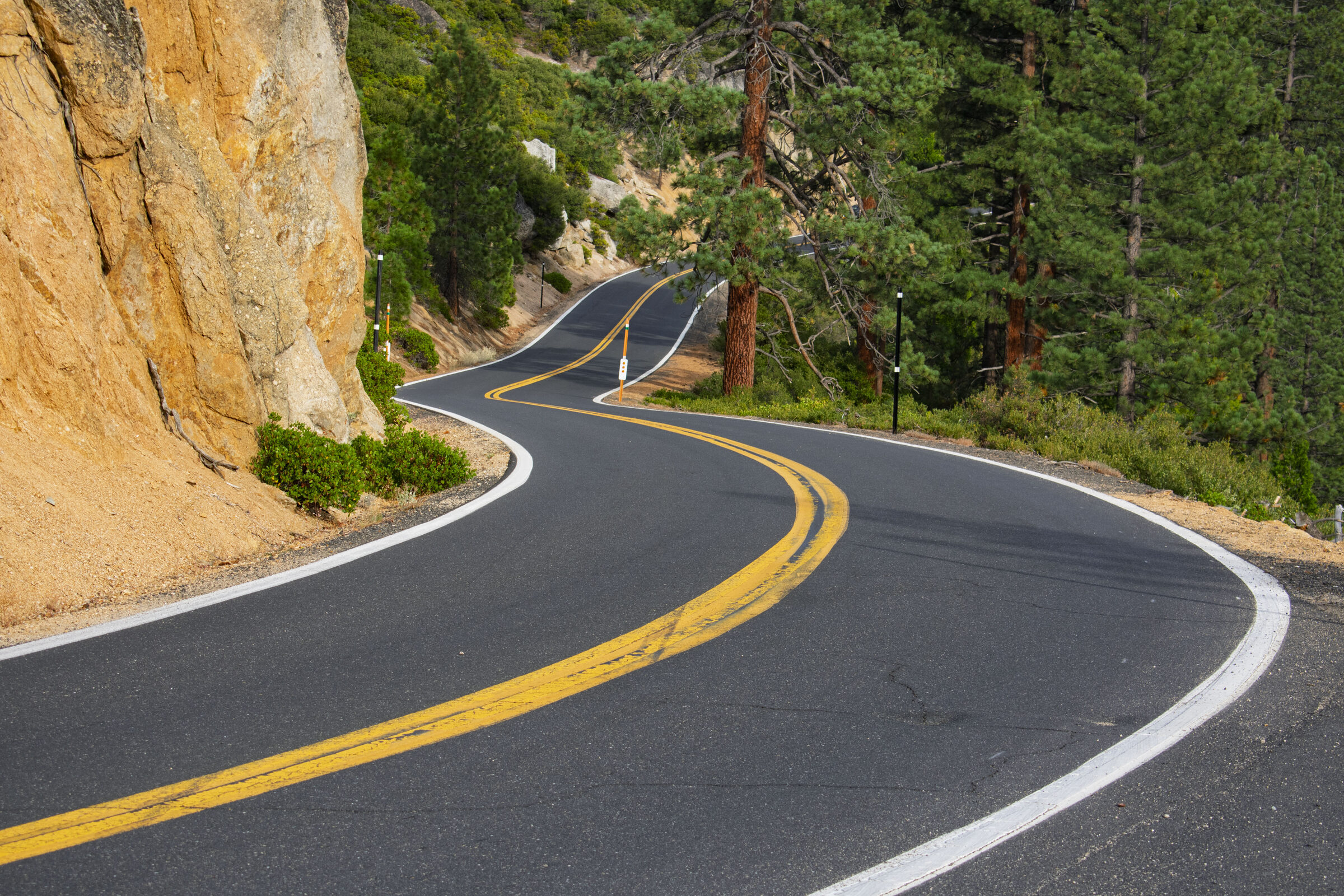 Highway 108 bending around a golden granite cliff with pines above